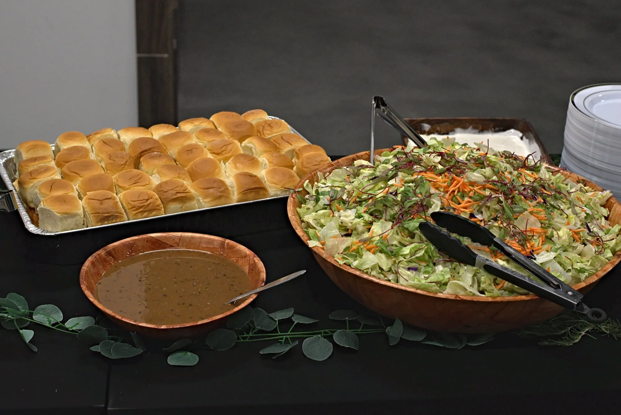 Slider rolls, salad and a bowl of dressing on the buffet with greenery tucked between the dishes