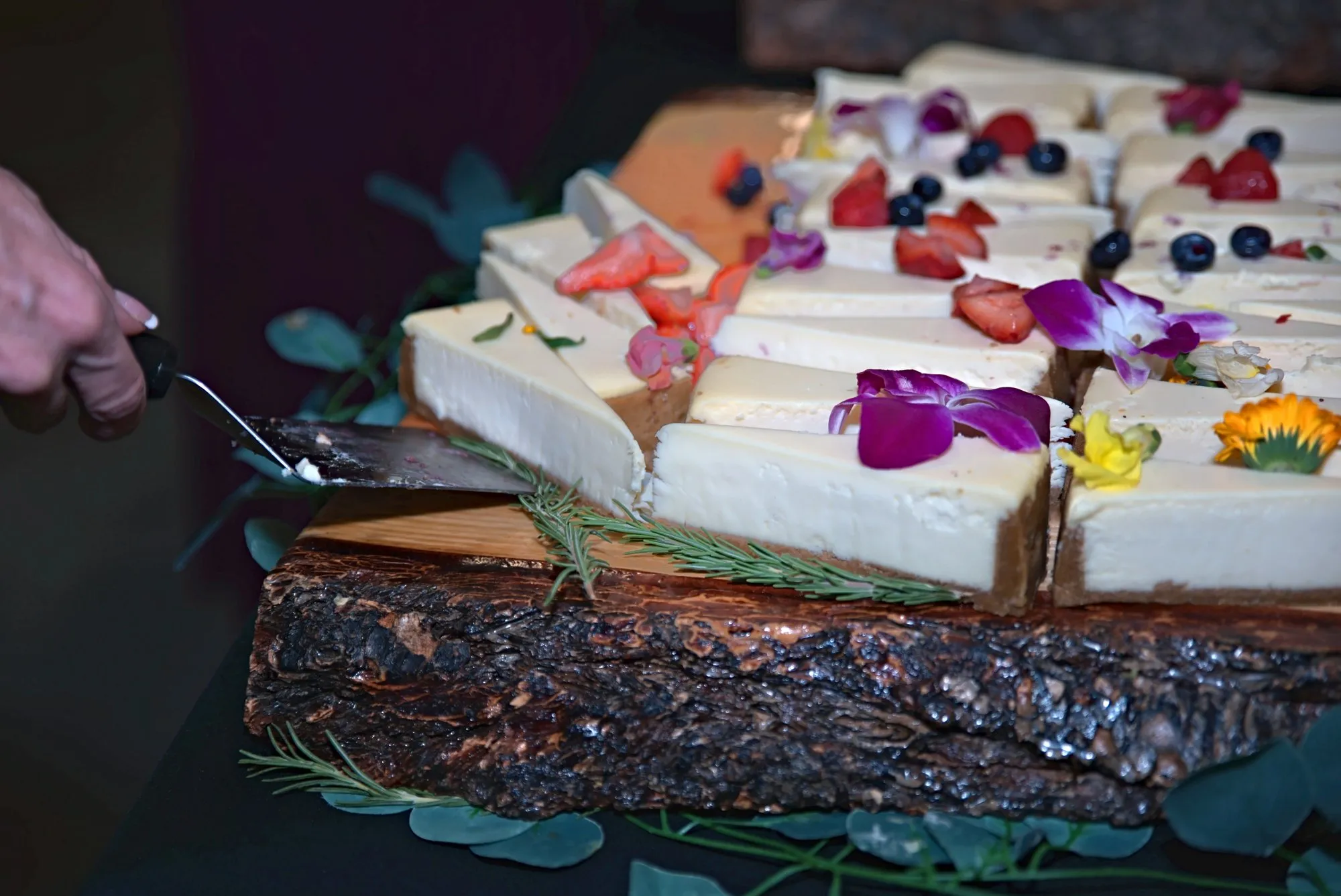 Cheesecake squares topped with berries and edible flowers on a live-edge wooden board
