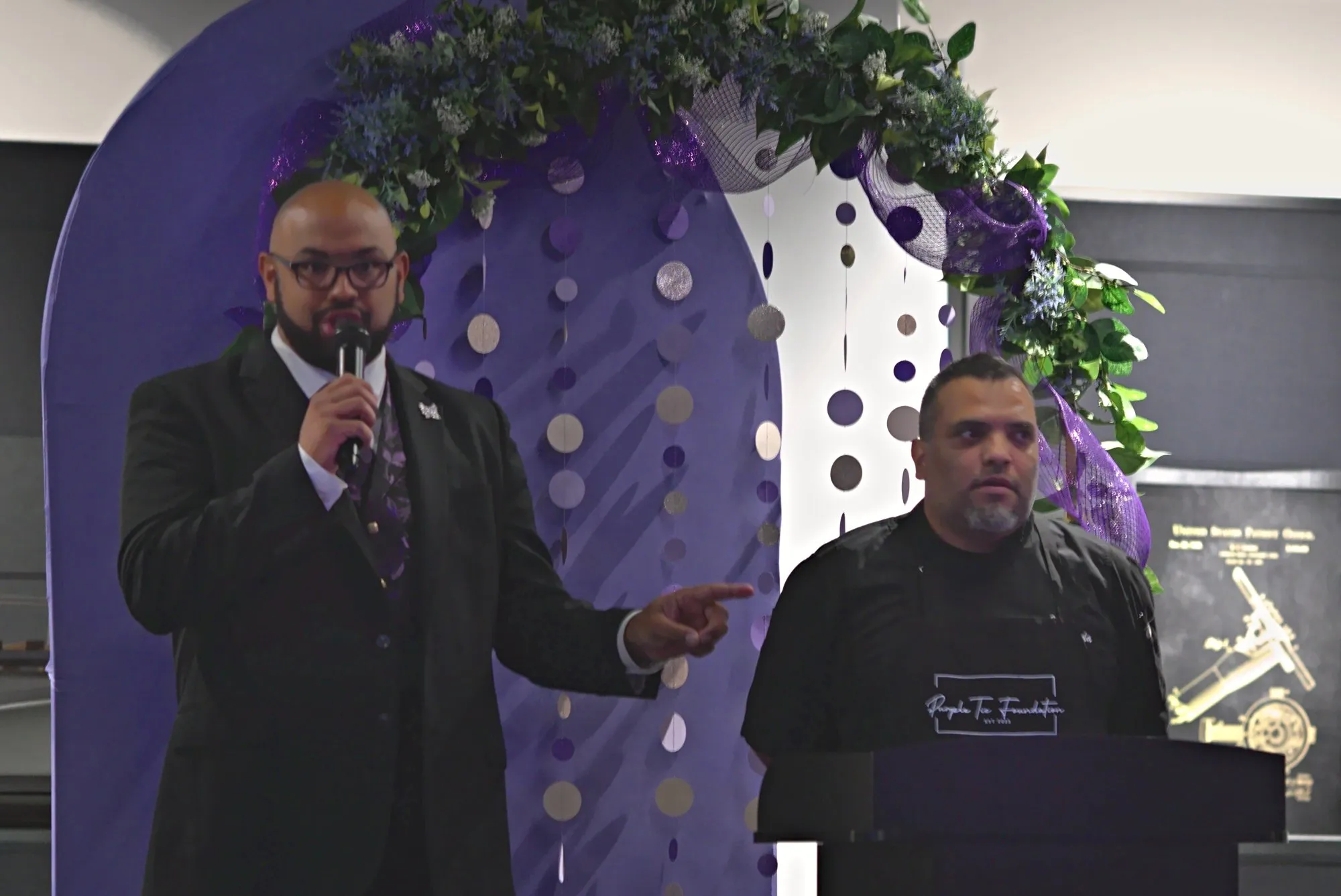 The chef beside the emcee at the podium under the floral arch