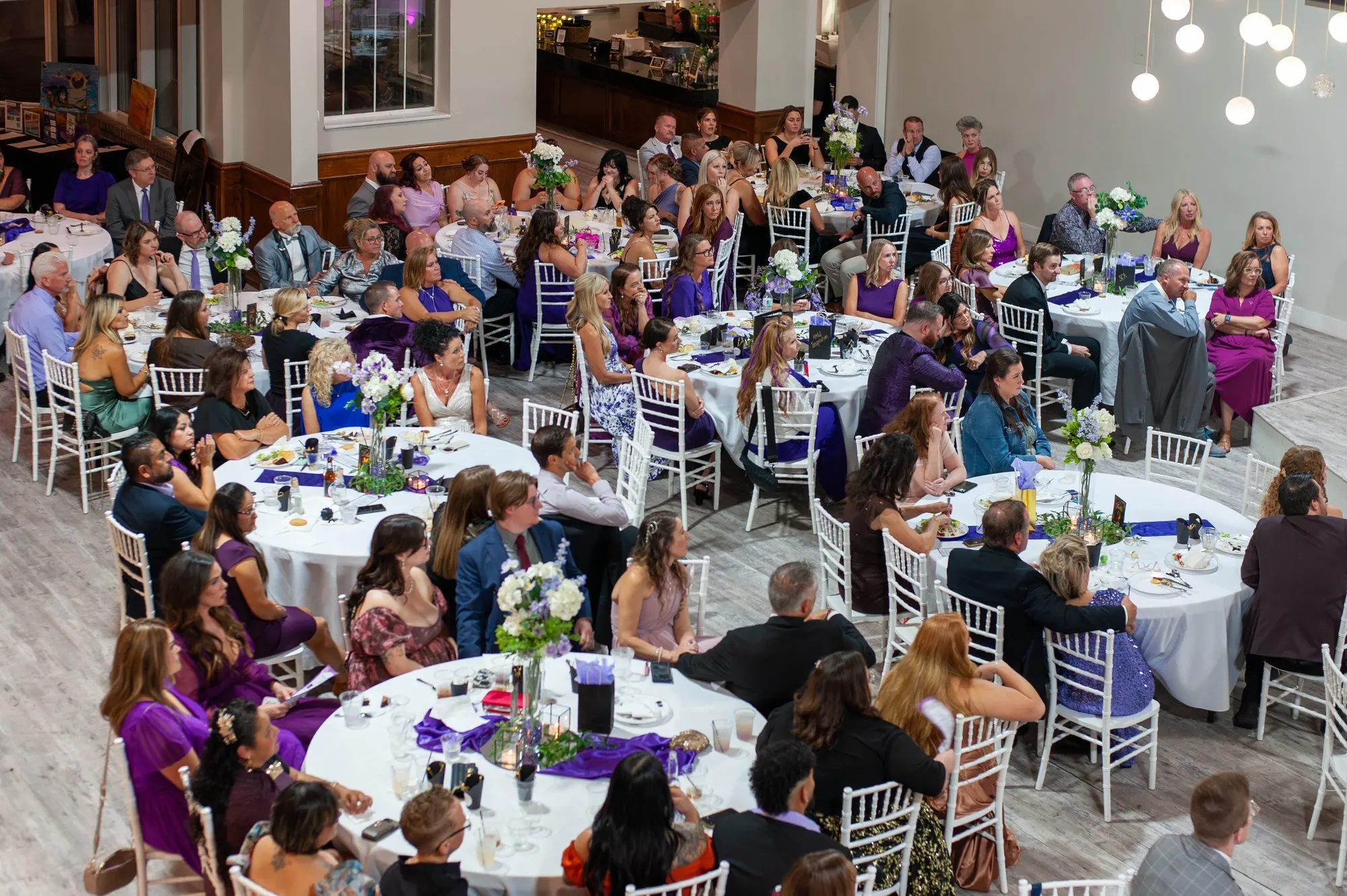 A full gala dining room from above, round tables dressed in white and purple during dinner