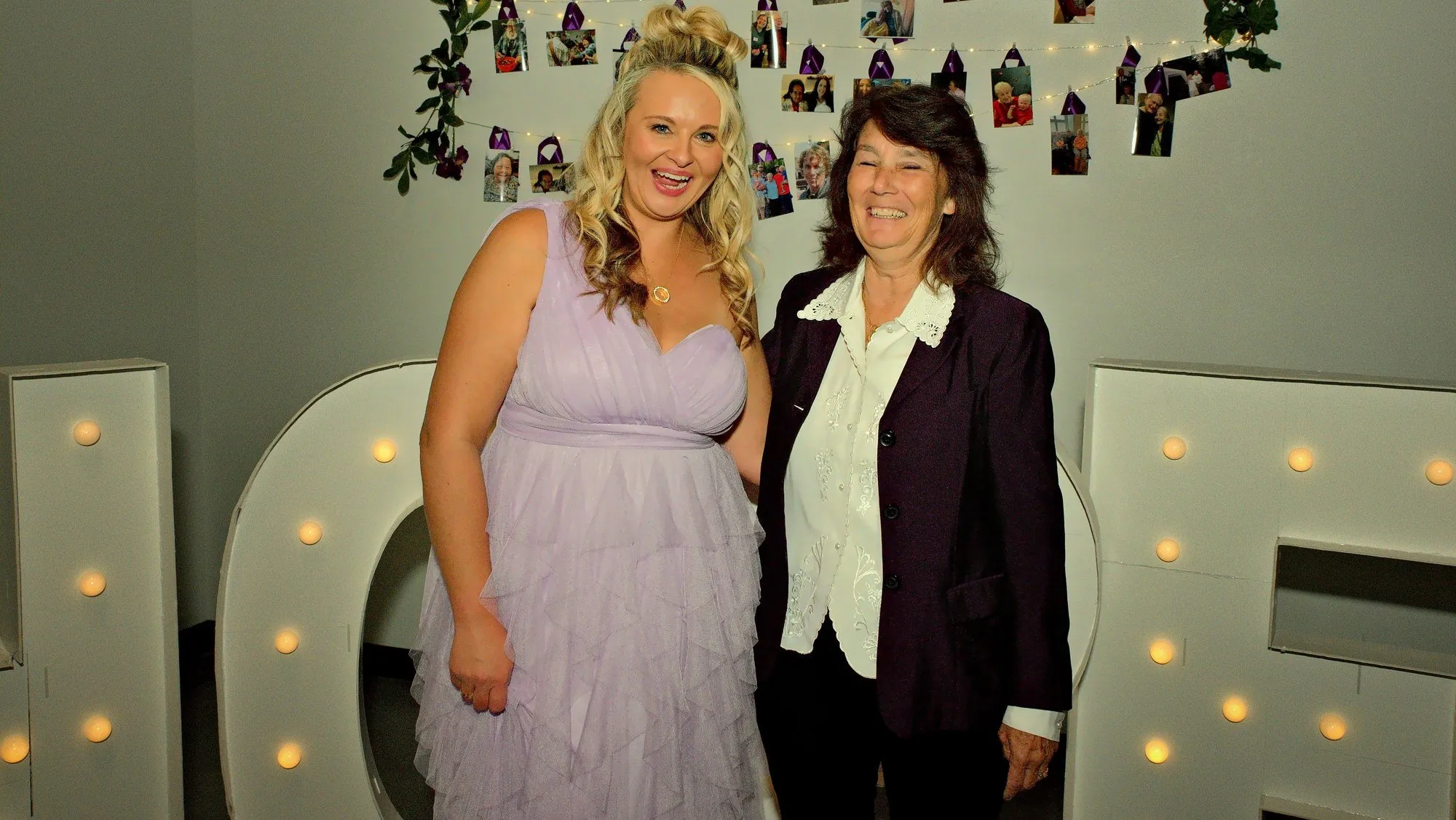 Two women laughing together in front of the lit HOPE letters at a gala
