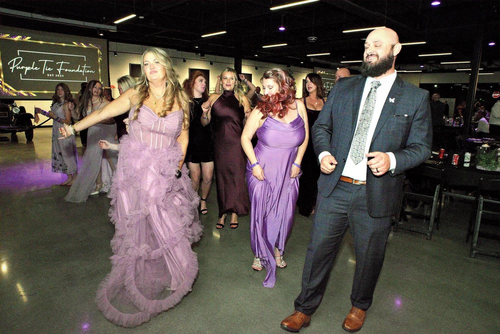 A couple dancing in a purple spotlight with the room blurred behind them