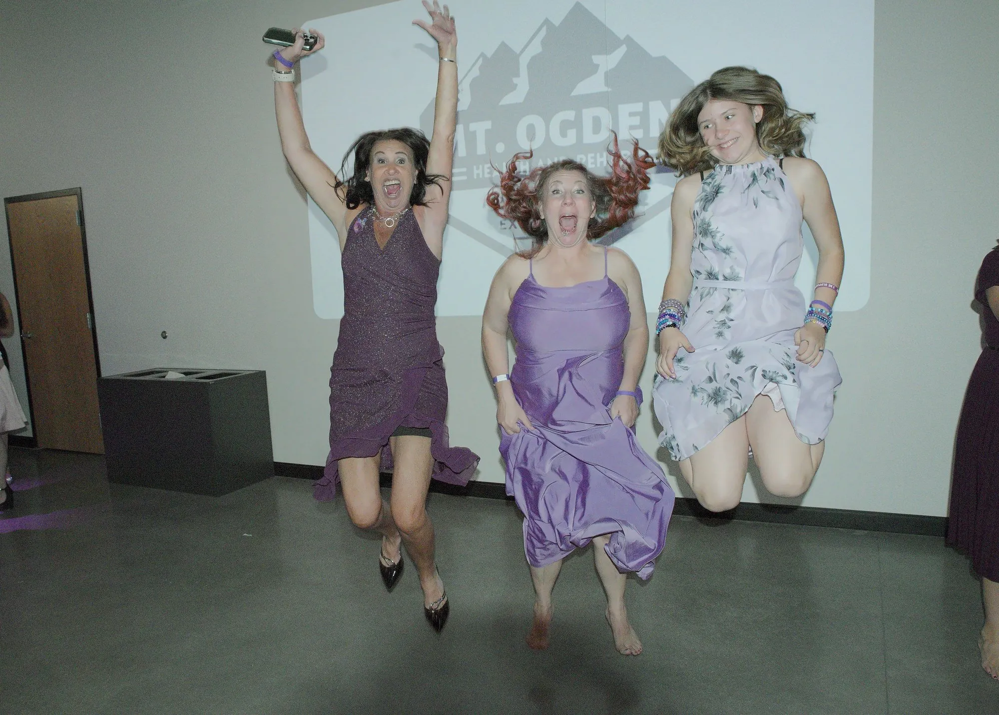 Three guests mid-jump in front of a projected sponsor logo