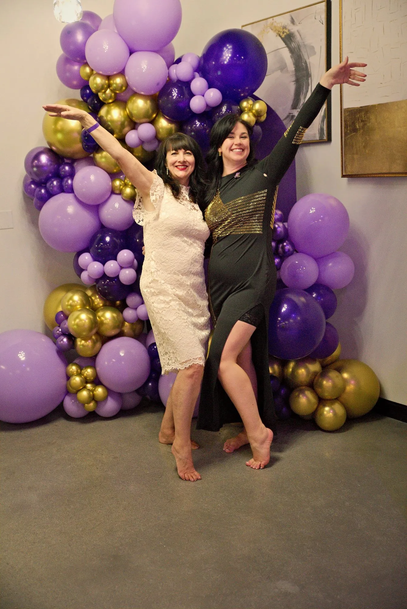 Two guests throwing their arms up at the balloon arch
