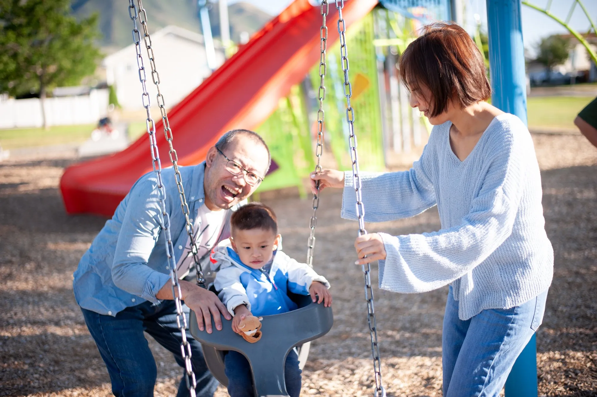 Mother pushing her giggling son on a red playground swing