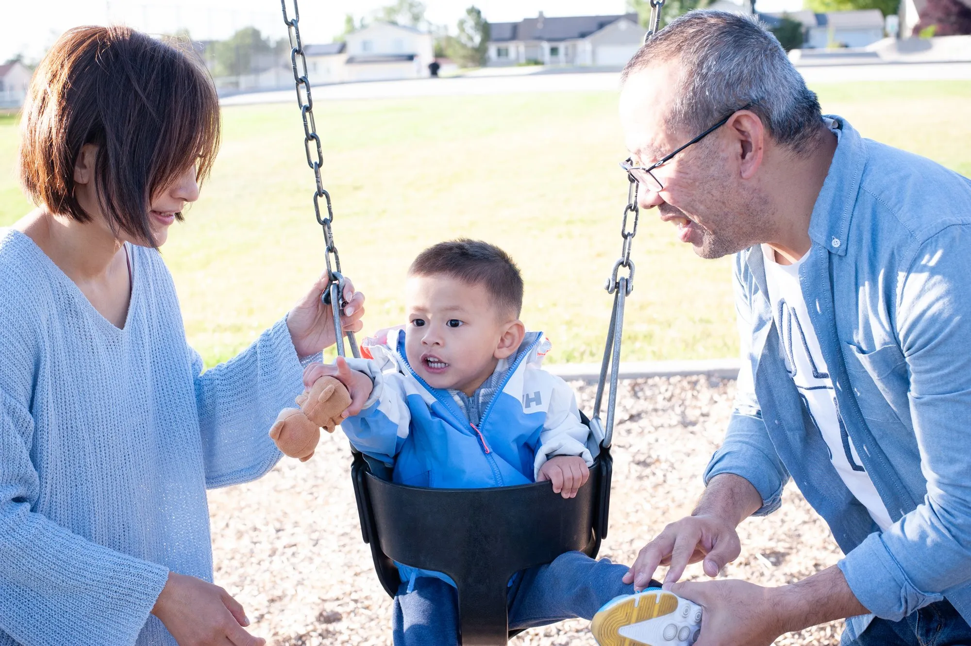 Grandfather and toddler grandson side by side on the swings