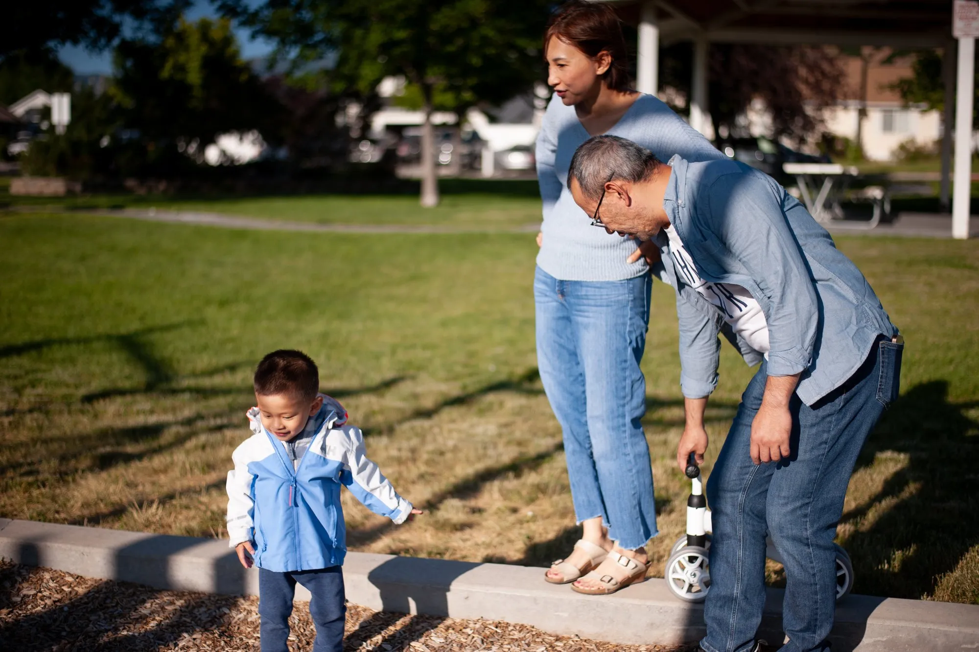 Toddler walking toward his parents across the park grass