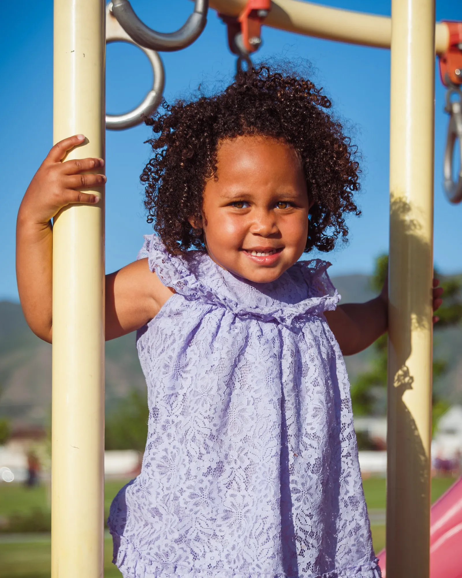 Young girl in a lilac dress smiling from the playground climbing frame