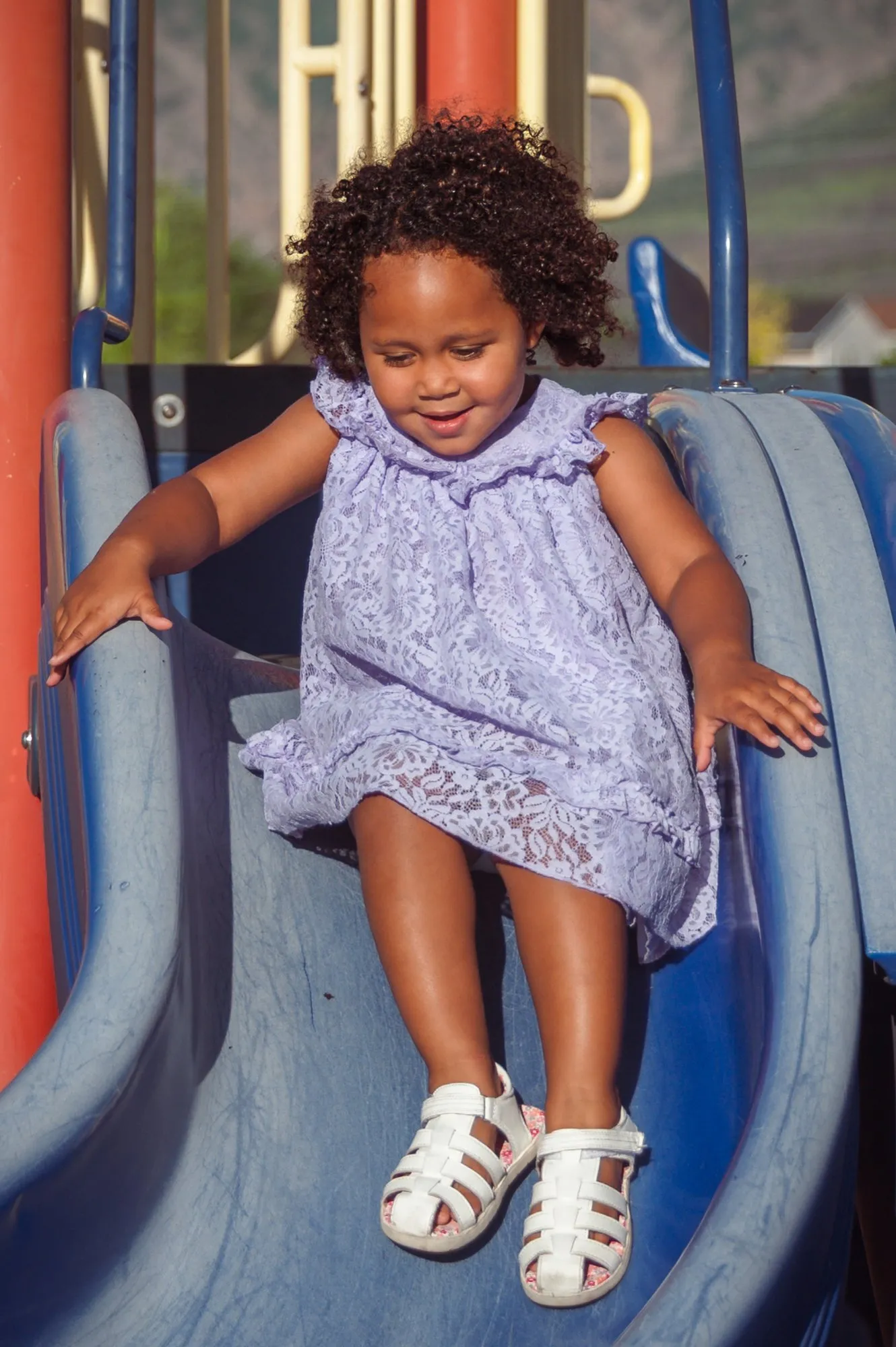 Girl in a lilac dress coming down the playground slide